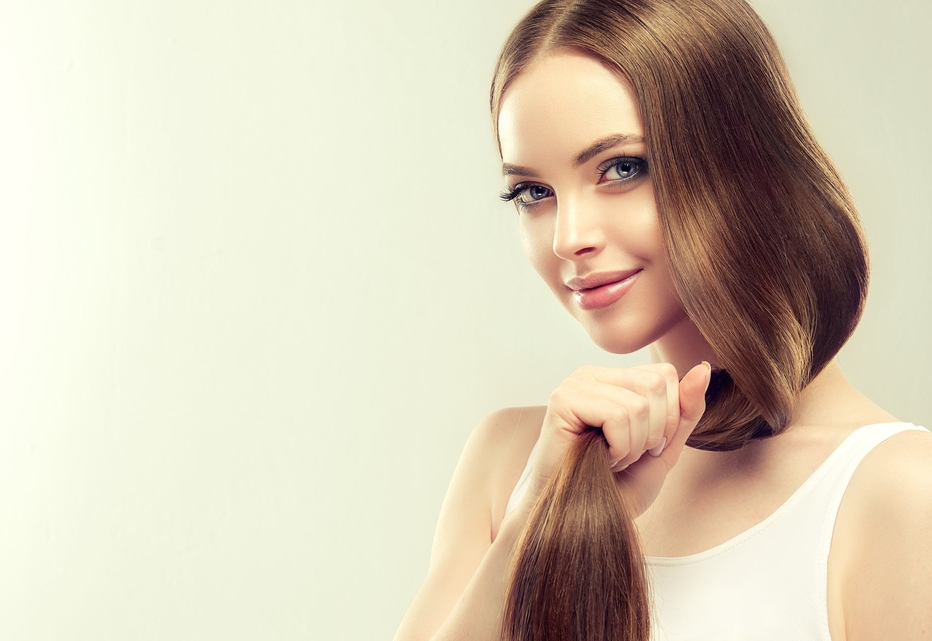 Young, brown haired beautiful model with long, straight hair is holding tail of well groomed and healthy hair in the hand.